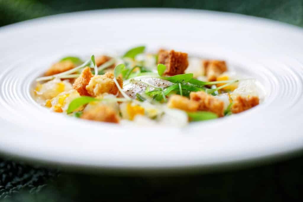 Salade légère et colorée avec croûtons et fromage, soigneusement disposée dans une assiette blanche sur un fond verdoyant.